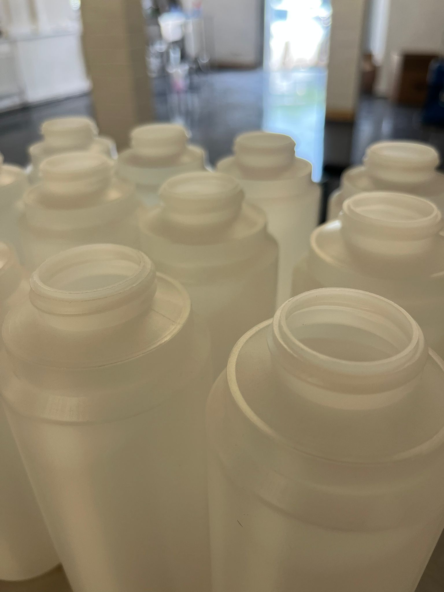 Empty food-grade HDPE bottles staged on stainless bench before filling.