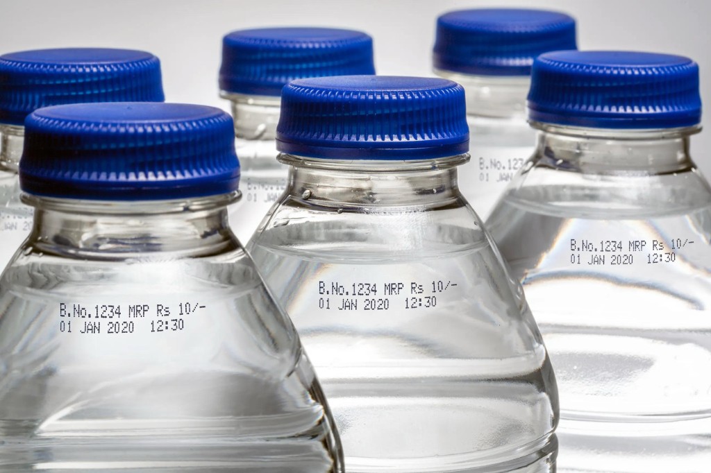 Clear PET bottles with blue caps showing CIJ batch and date coding around the neck.
